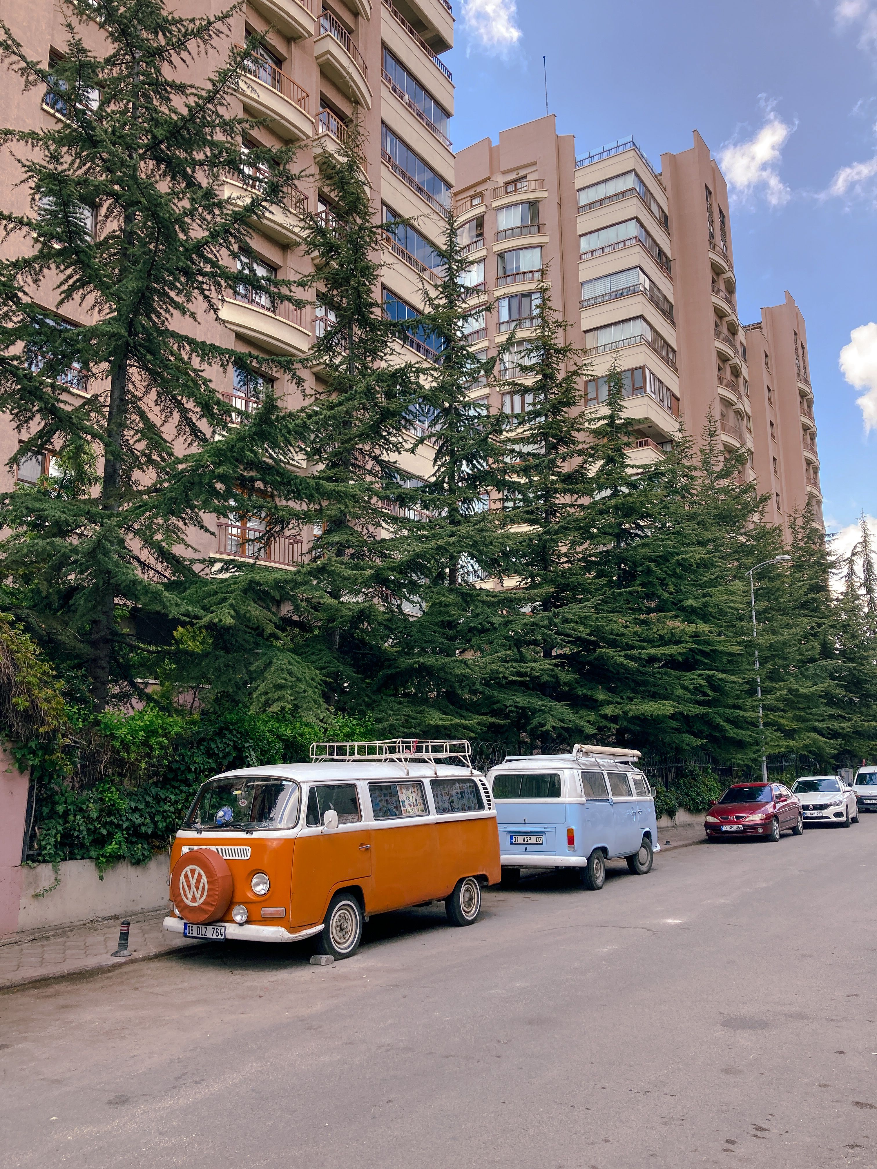 Two vintage Volkswagen vans parked on a city street surrounded by tall residential buildings and trees.