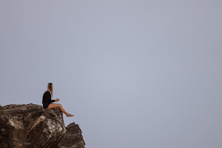 Blonde Woman With Drink Sitting On Rocks Edge