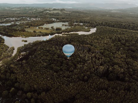 Captivating aerial shot of a hot air balloon floating over lush forests and a winding river in Brunswick Heads, NSW, Australia.