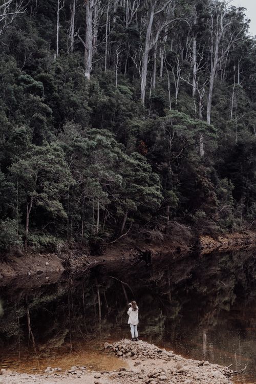 Free A person stands near a forest pond with a reflection, capturing Tasmania's serene wilderness. Stock Photo