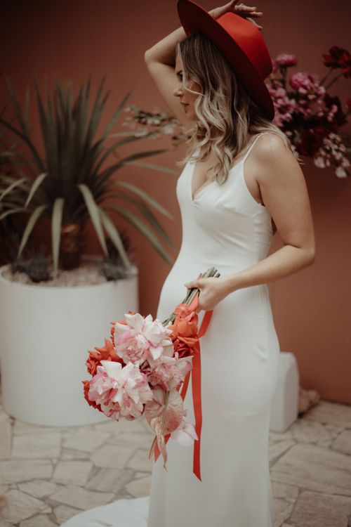 Free Stylish bride posing with a vibrant floral bouquet and red hat outdoors. Stock Photo