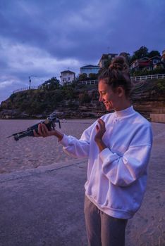 A woman with a drone in a tranquil outdoor beach setting at twilight, enjoying leisure time.