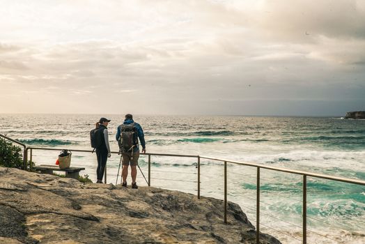 A couple stands on a rocky shore, enjoying the ocean view on a cloudy day.