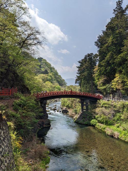 Free Picturesque footbridge spanning a tranquil river surrounded by lush forest and hills. Stock Photo