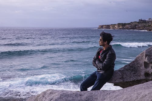 Man Leaning on Rock Near Beach Shore