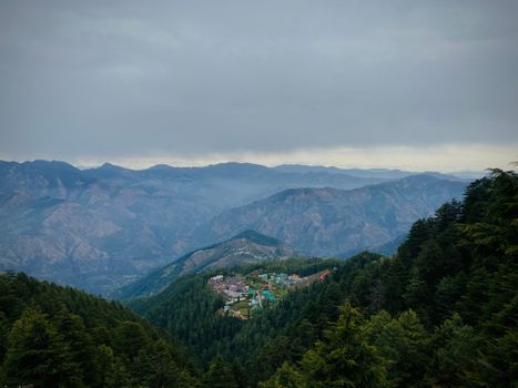 A serene view of a village nestled in the evergreen Shimla hills under overcast skies.