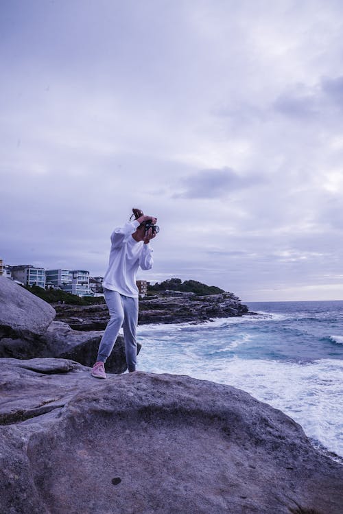 Gratis Pria Mengambil Foto Laut Saat Berdiri Di Atas Batu Foto Stok