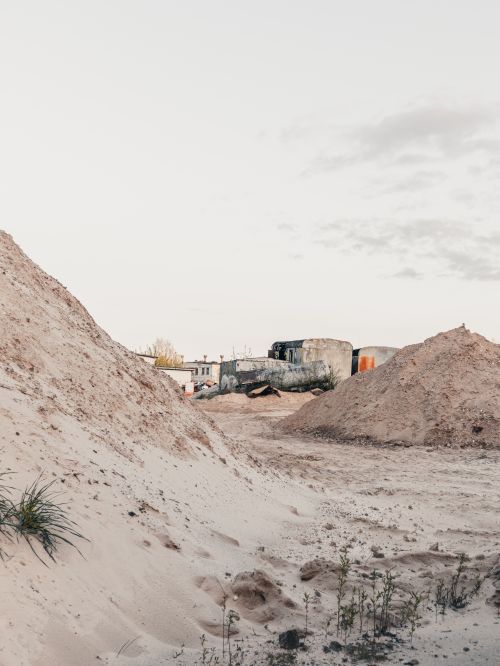 Free A serene desert expanse with sand dunes and deserted buildings under a pale sky. Stock Photo