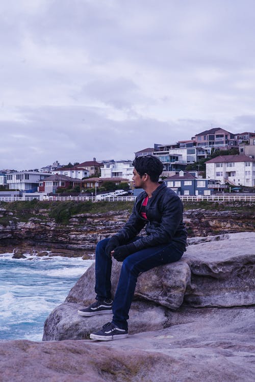 Free Man Sitting on Rock Near in Front of Ocean Water Stock Photo