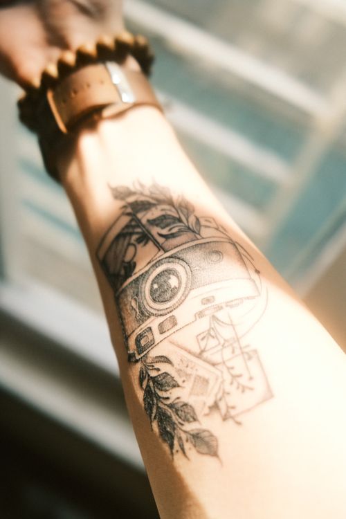 Free Artistic closeup of a tattooed arm featuring a camera design along with a wristwatch. Stock Photo