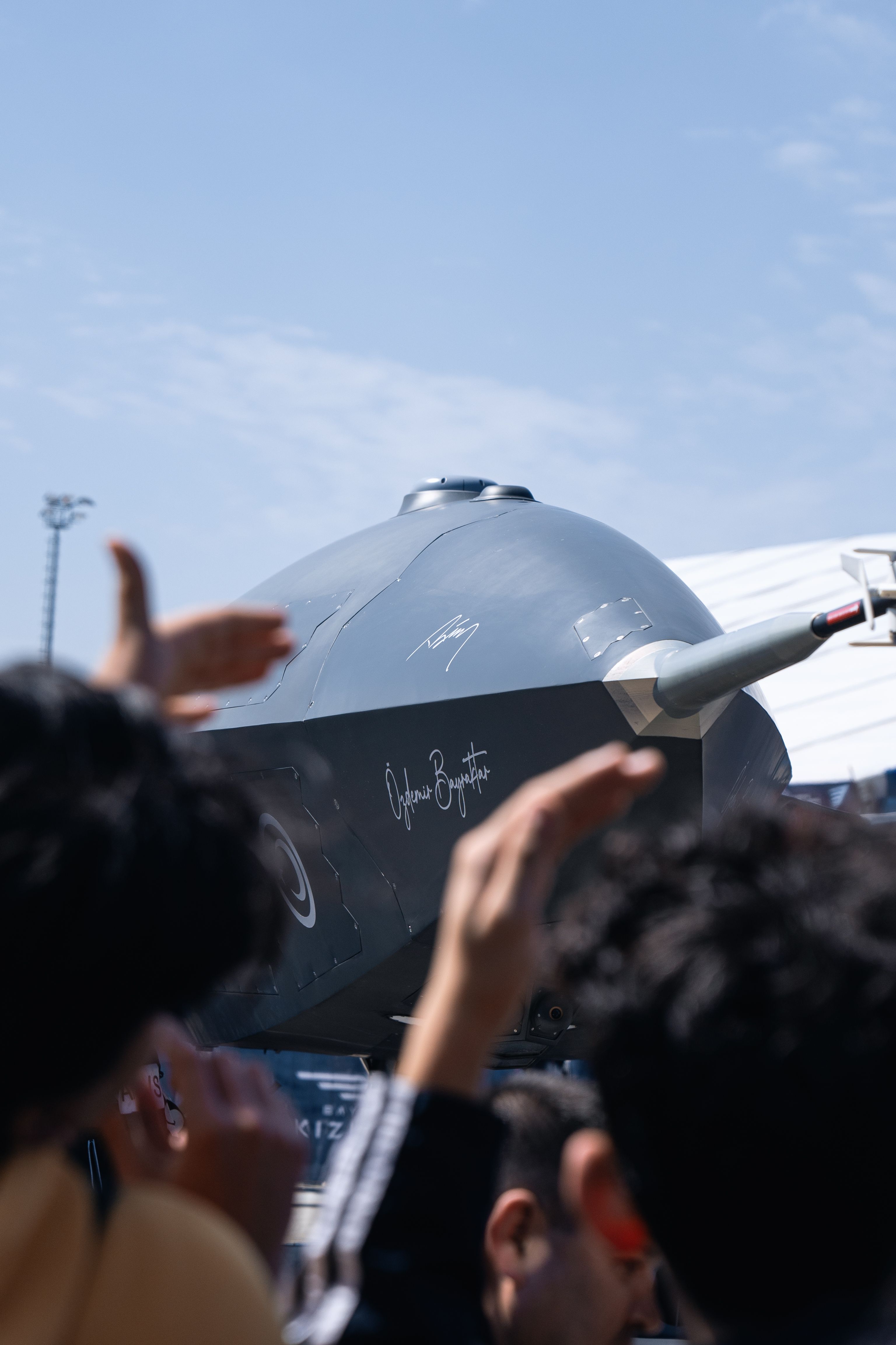 A close-up shot of a jet aircraft with visible spectators in the foreground during a daytime event.
