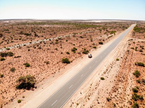 Free Aerial shot of a long road cutting through an arid desert landscape under a clear blue sky. Stock Photo