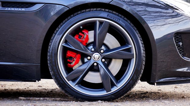 Detailed close-up of a Jaguar car wheel with sleek black alloy design and red brake caliper.