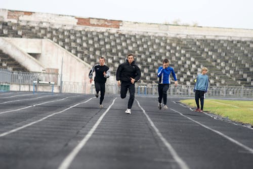 Four people running on a track in an empty stadium
