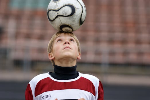 A young soccer player skillfully balances a ball on his head during outdoor practice.