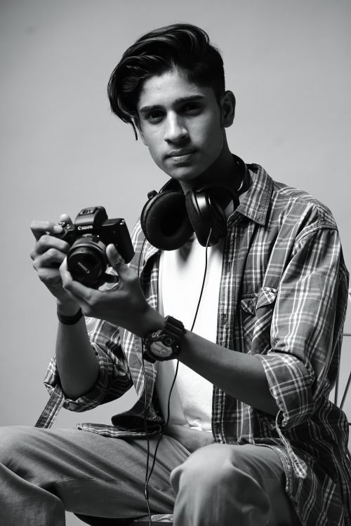 Free Black and white portrait of a young man with a camera and headphones in a studio setting. Stock Photo