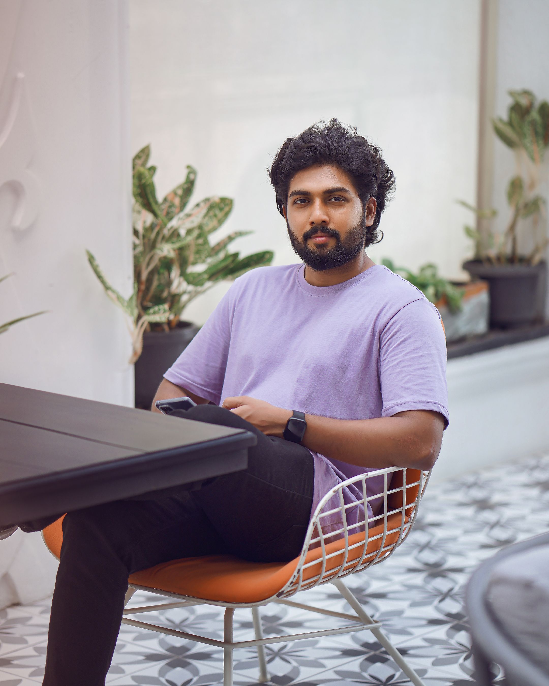 Man in a purple t-shirt sitting indoors with plants and modern decor.