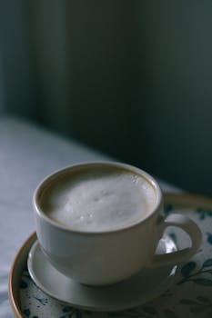 Ceramic cup filled with frothy cappuccino on a patterned saucer in soft lighting.
