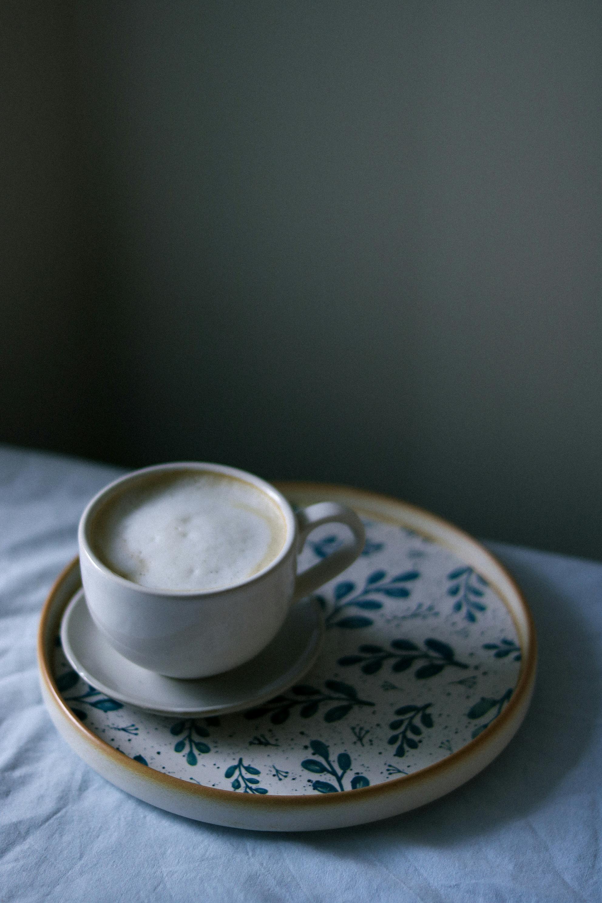 A warm cappuccino served in a ceramic cup on a decorative saucer indoors.