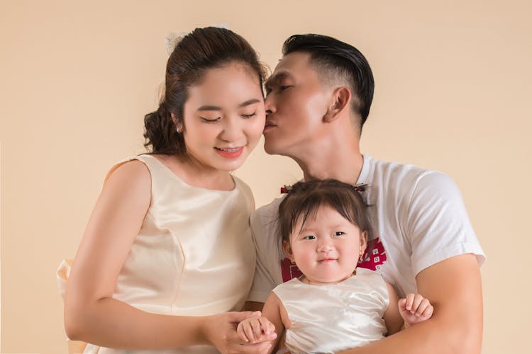 Man Kissing Wife And Holding Child In Hands