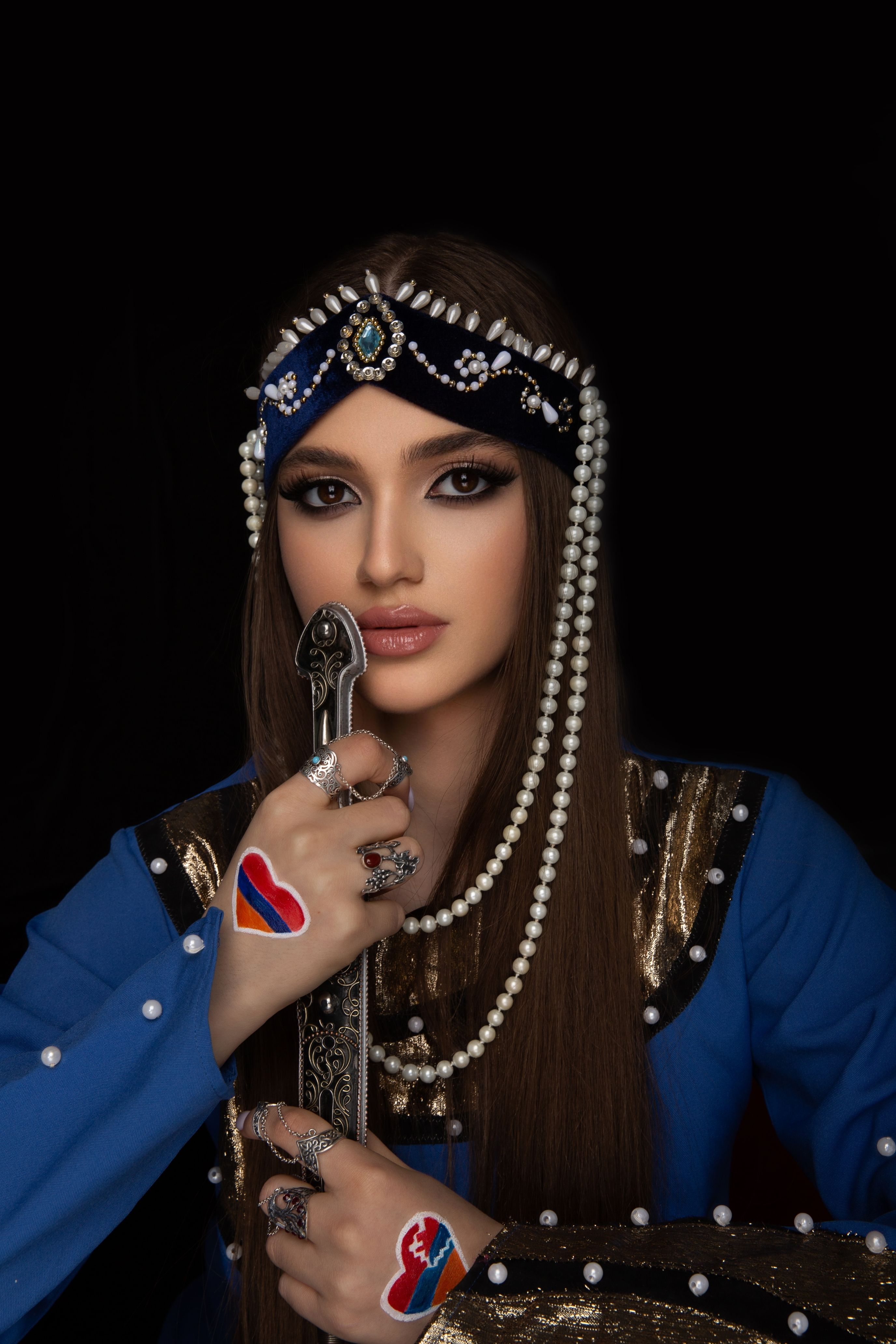 Portrait of an Armenian woman in traditional attire, adorned with jewelry and holding a sword.