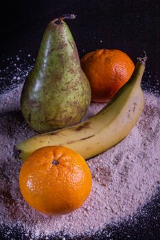 Artistic arrangement of pear, banana, and tangerines on textured surface. Vibrant colors and moody lighting.