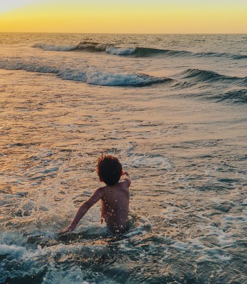 Free A young boy joyfully plays in the ocean waves during a golden sunset, capturing a moment of vacation bliss. Stock Photo