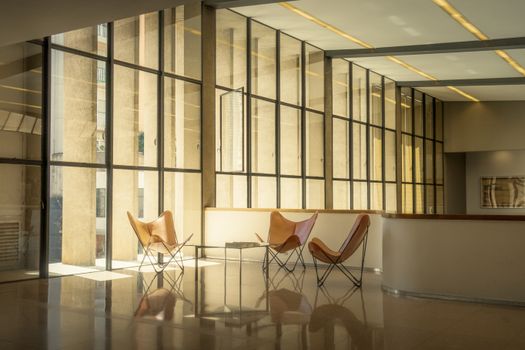 Spacious office lounge with modern design and natural lighting, featuring glass windows and leather chairs.
