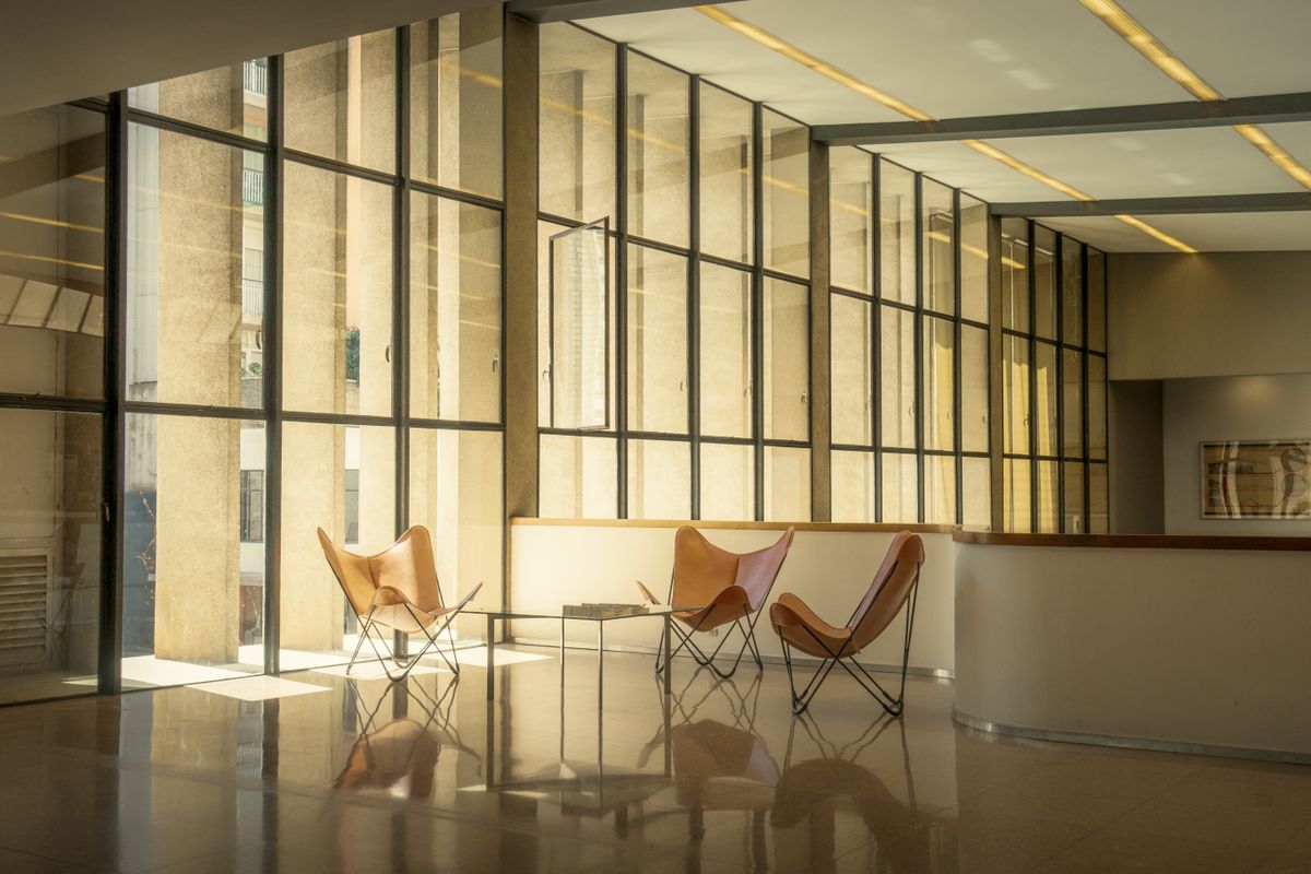 Office waiting area with leather lounge chairs, a small table, and floor-to-ceiling windows providing warm natural light