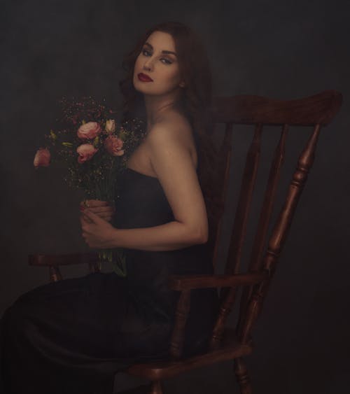 Portrait of a Young Woman Sitting on a Chair and Holding a Bouquet of Roses 