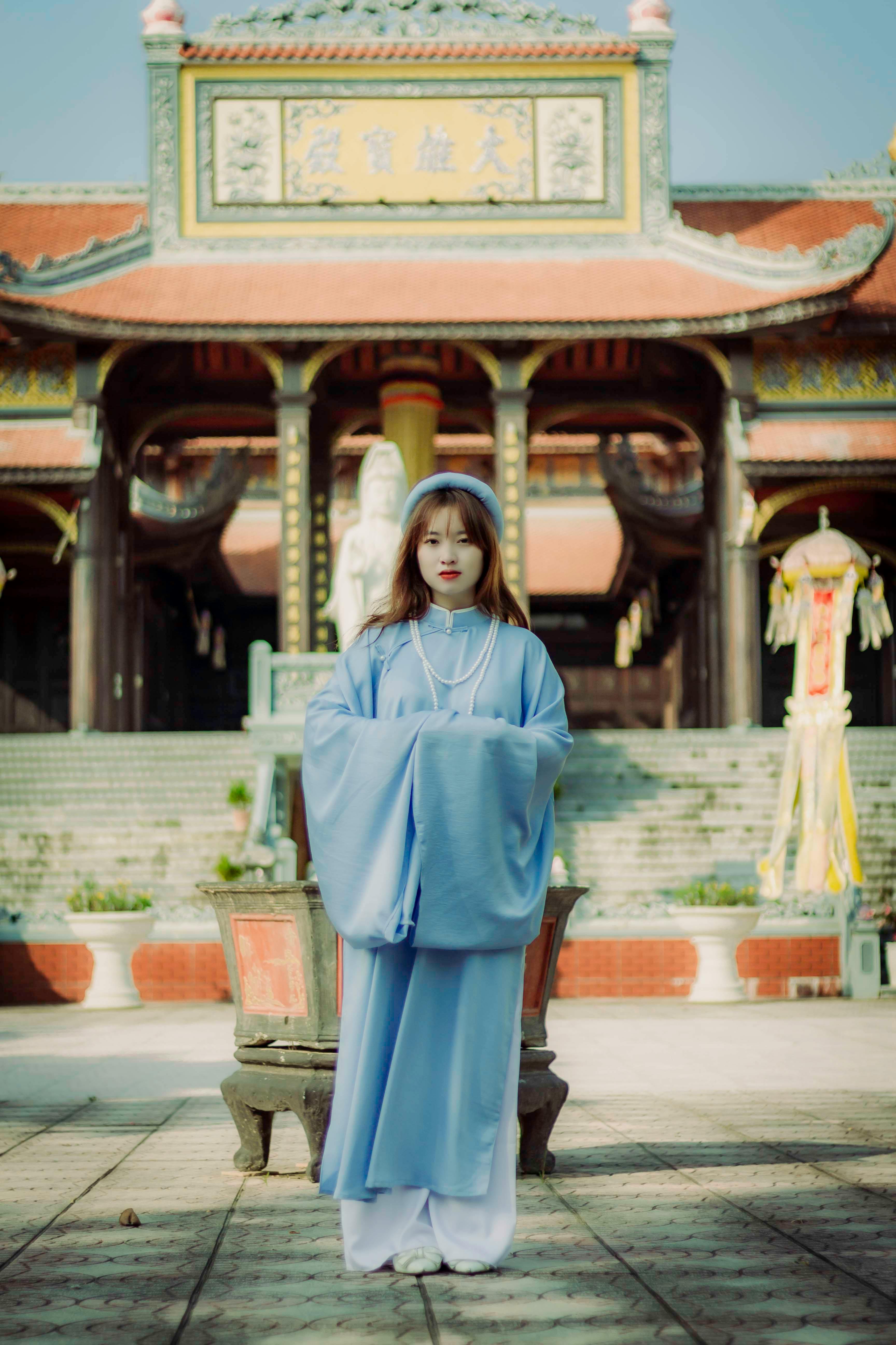 A woman in blue stands gracefully in front of an ornate temple, showcasing traditional fashion.
