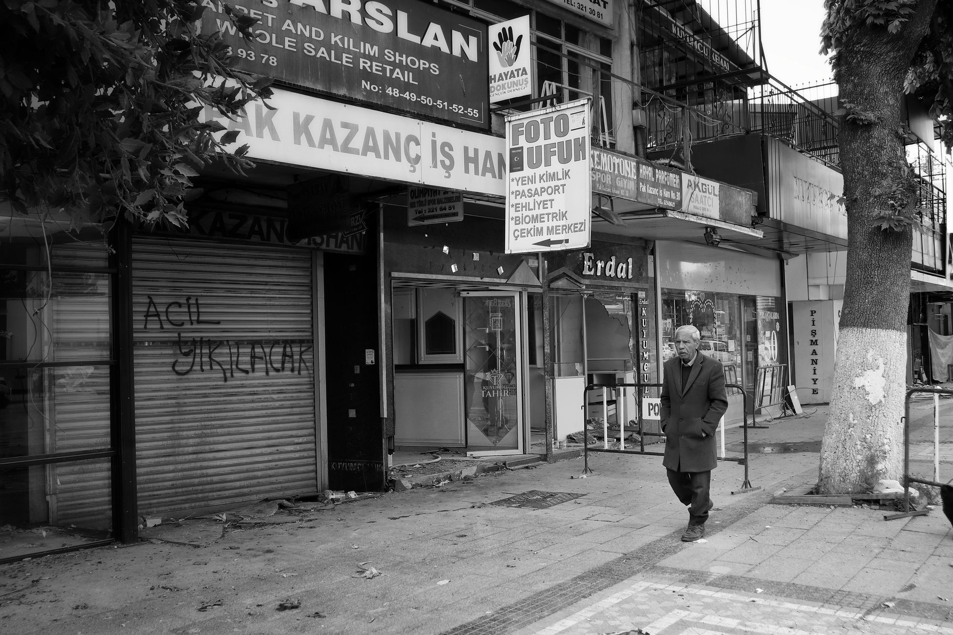 Black and white photo of a man walking on an empty city street with shops.
