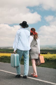 A couple walks down a rural road carrying suitcases, enjoying a journey together.