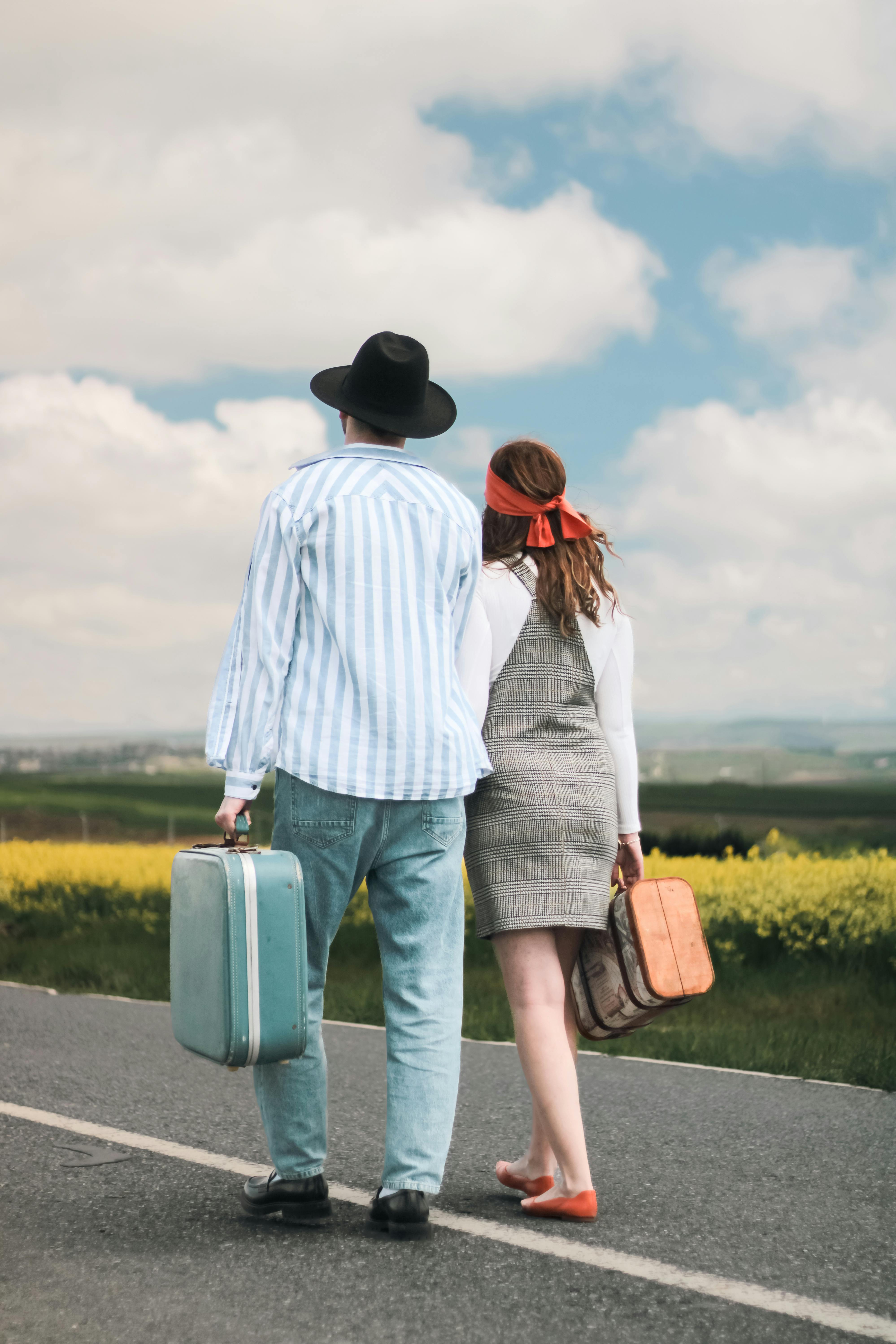 Free A couple walks down a rural road carrying suitcases, enjoying a journey together. Stock Photo