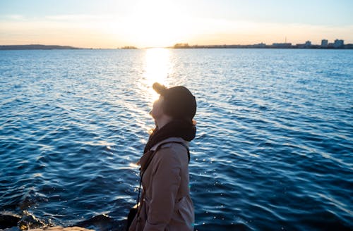 Sunlight over Woman Posing in Cap and Jacket on Shore