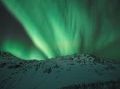 夜晚，北极光照亮了白雪皑皑的山峰，景色壮丽