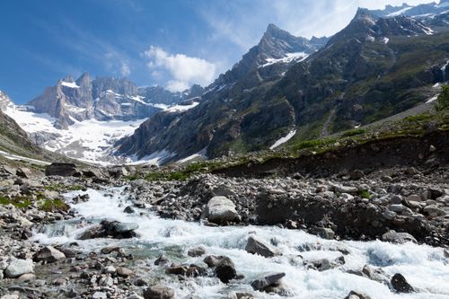 Free Breathtaking view of a mountain stream flowing through majestic alpine terrain under a clear blue sky. Stock Photo