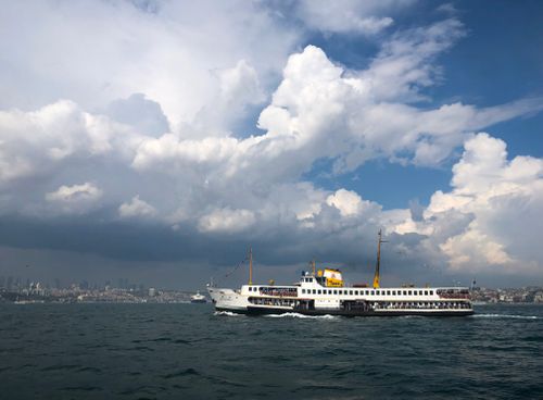 Free Ferry crossing the Bosporus in Istanbul under dramatic cloudy skies, embodying scenic travel. Stock Photo