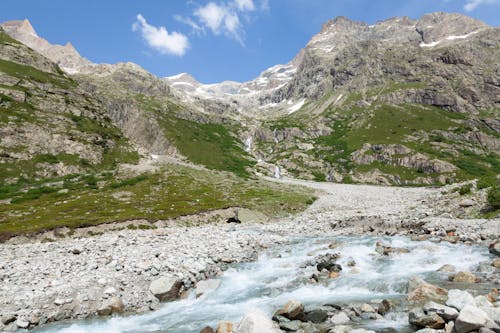 Alpine Landscape with View of a Stream and Mountains under Blue Sky 