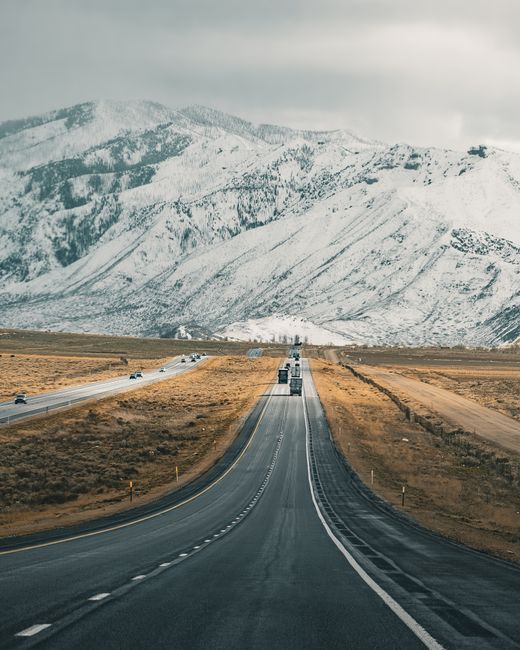 A scenic winter highway leading towards snowcapped mountains under a cloudy sky.