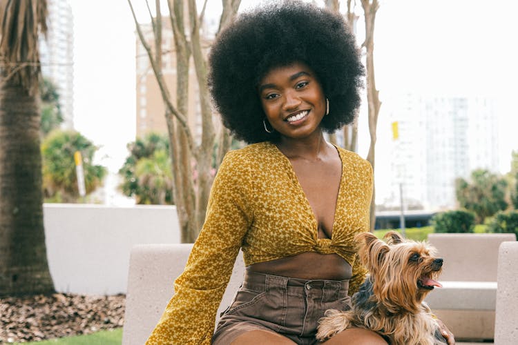 Young Woman In A Fashionable Summer Outfit Sitting With Her Little Dog And Smiling 