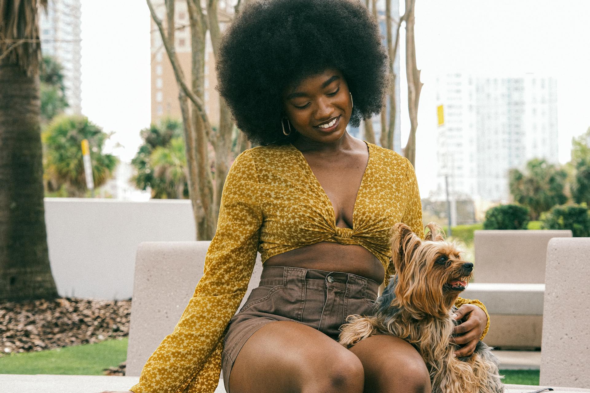 Young Woman in a Fashionable Summer Outfit Sitting with Her Little Dog and Smiling