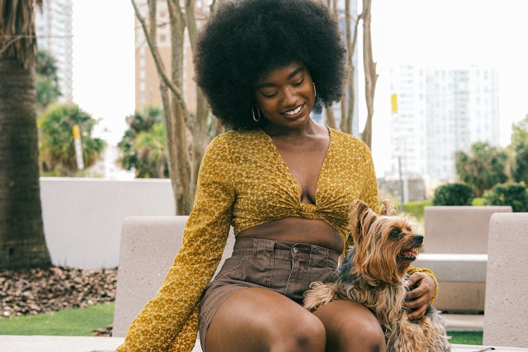 Young Woman In A Fashionable Summer Outfit Sitting With Her Little Dog And Smiling 