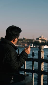 A man observes the sea while smoking near a coastal fence in Istanbul.