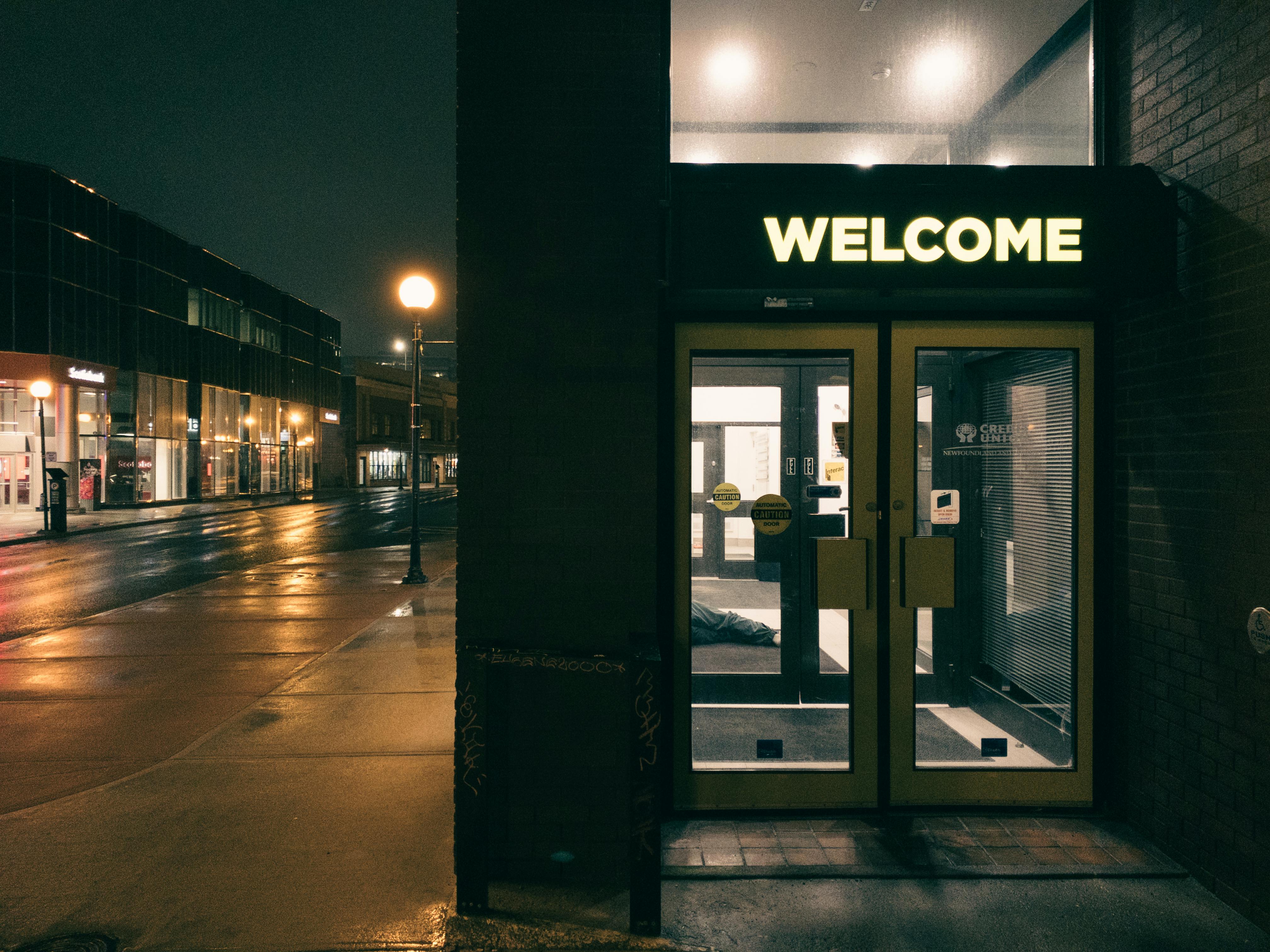 Moody nighttime street in St. John's, NL with warmly lit entrance and wet pavement.