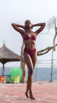 Graceful African woman in swimwear posing by a tropical beach with a serene backdrop.