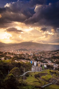A breathtaking urban landscape under dramatic clouds during sunset with mountains in the background.