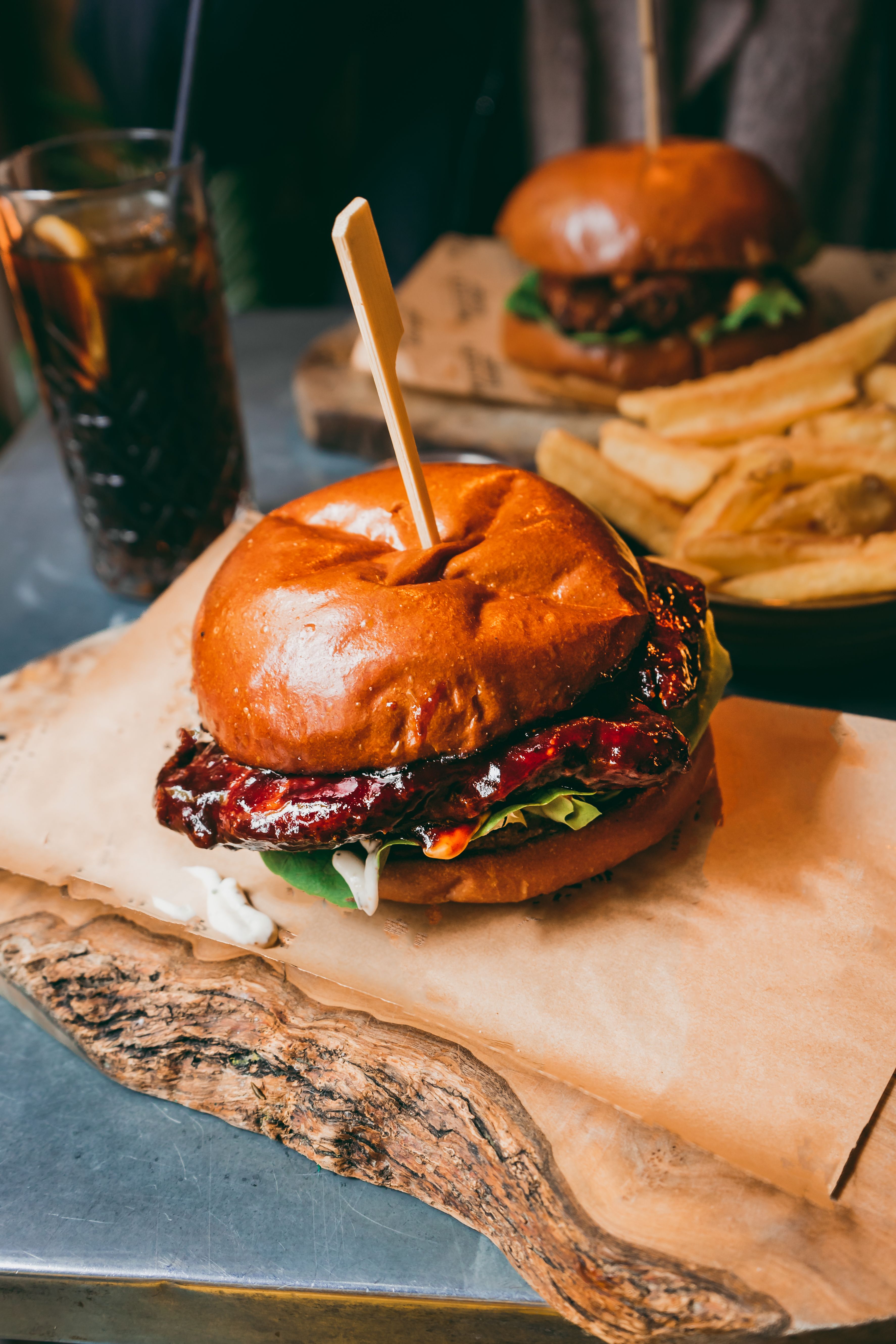 Delicious burger with lettuce and sauce served with fries and a cold drink in a restaurant setting.