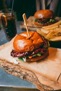 Delicious burger with lettuce and sauce served with fries and a cold drink in a restaurant setting.