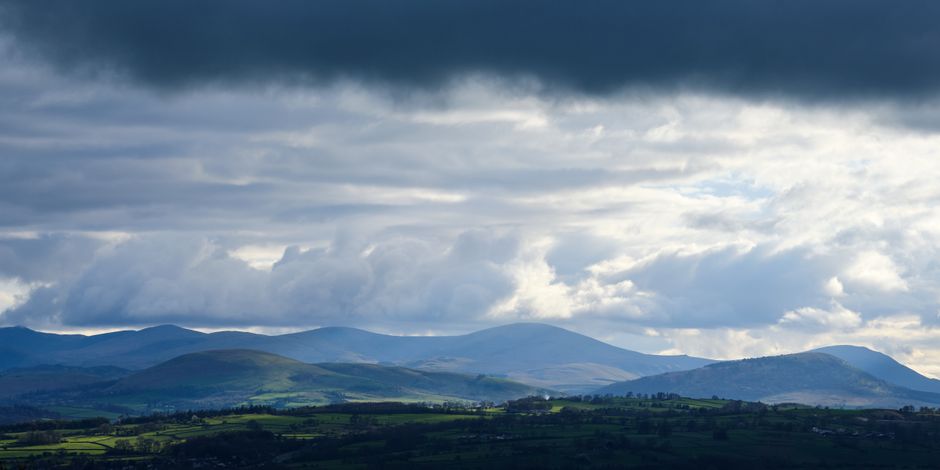 Fotomural Majestuoso cielo nublado sobre colinas verdes exuberantes en Penrith, Inglaterra, ofreciendo una vista paisajística serena.